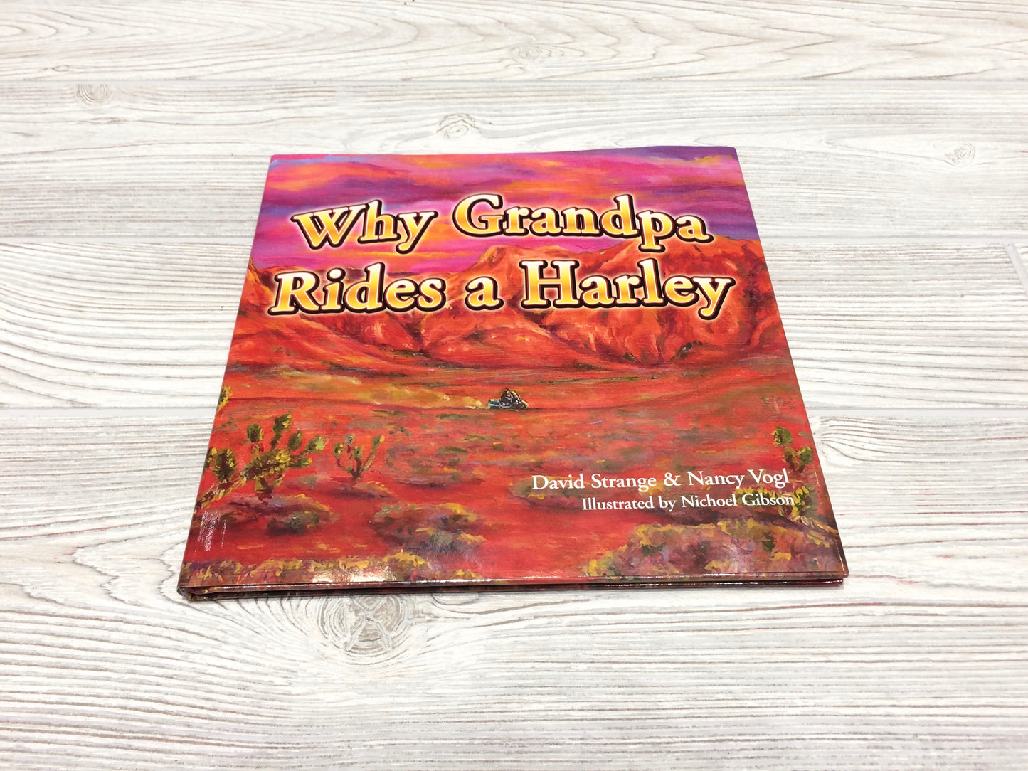 Hardcover book titled 'Why Grandpa Rides a Harley' with a colorful cover featuring a harley-davidson motorcycle in a desert landscape.