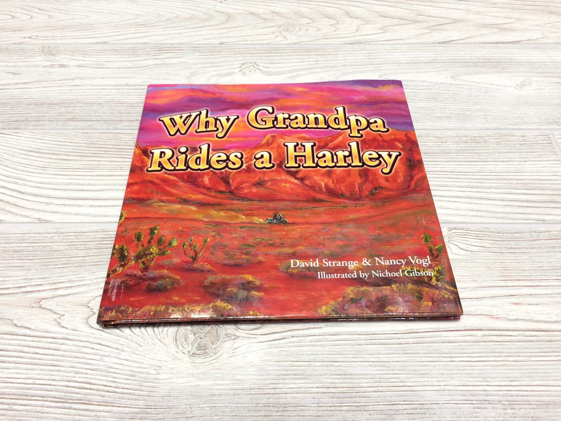Hardcover book titled 'Why Grandpa Rides a Harley' with a colorful cover featuring a harley-davidson motorcycle in a desert landscape.